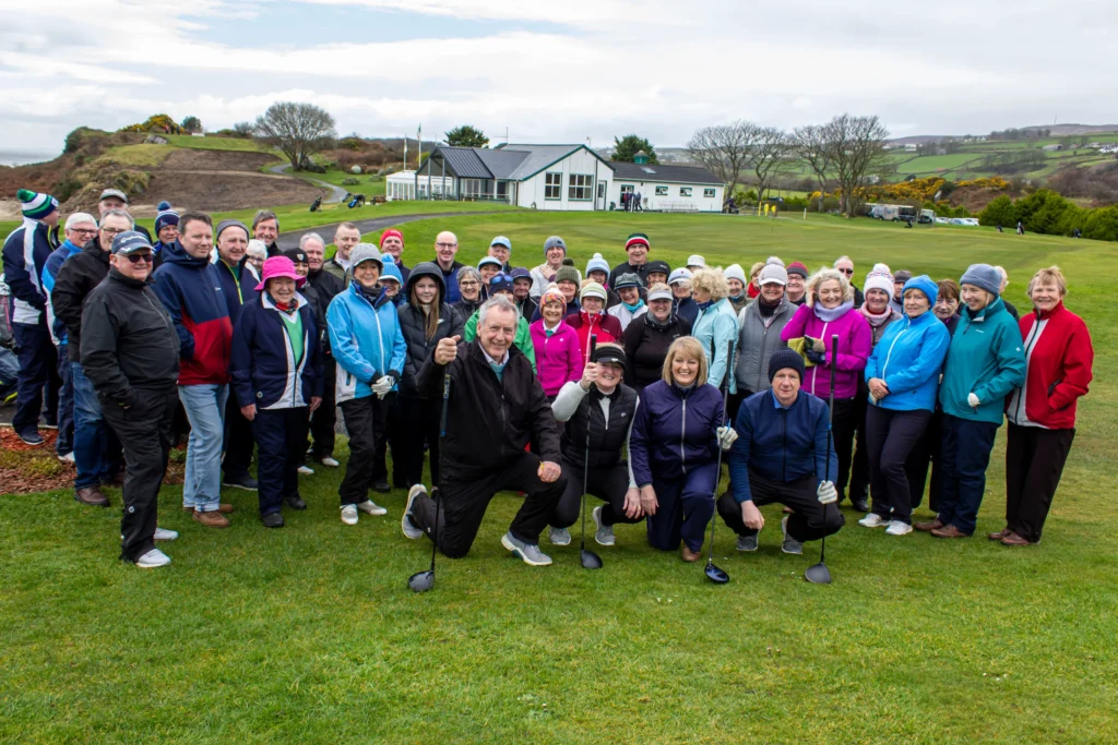 Large group of golfers on the green by the clubhouse, smiling in winter gear at an Irish golf club.