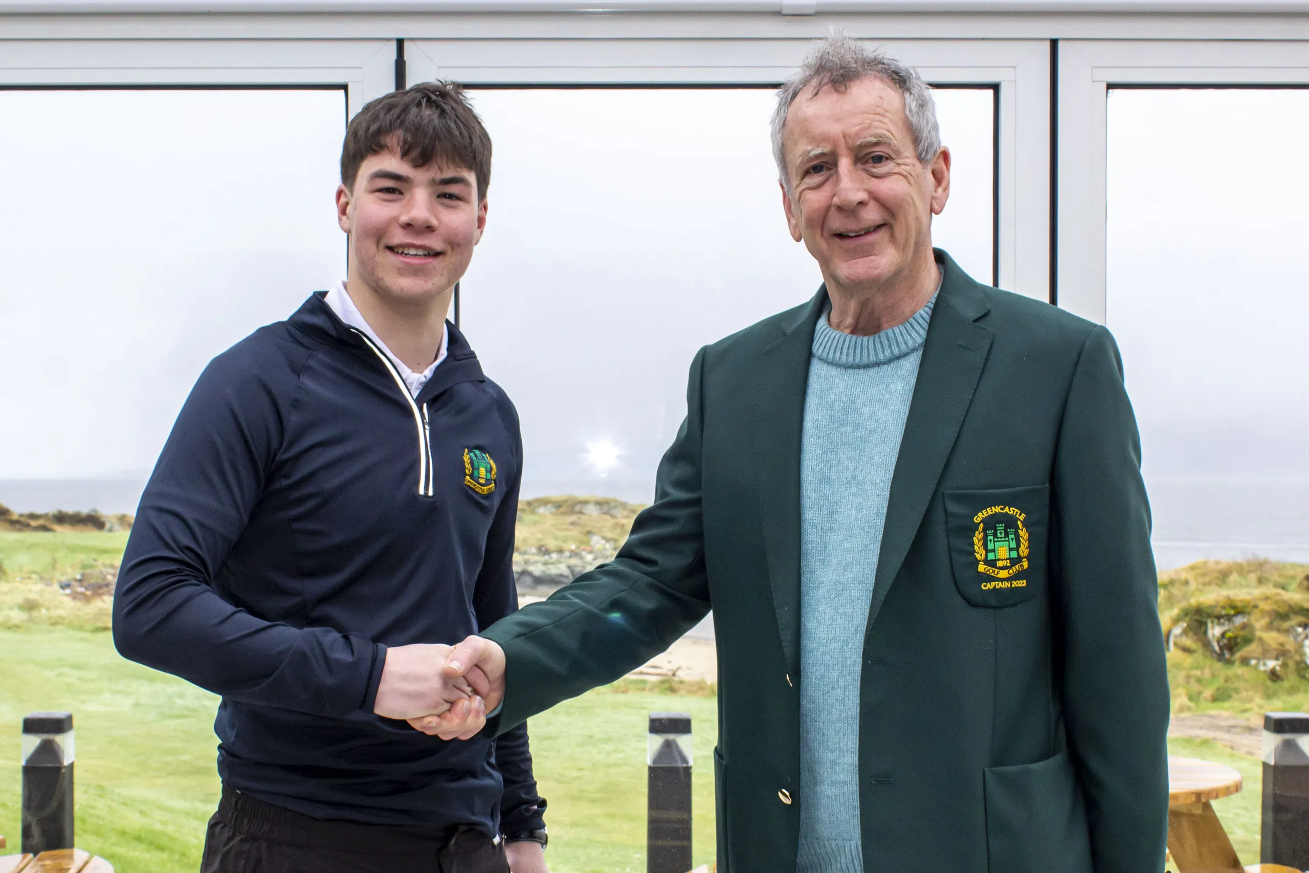 Greencastle Golf Club captain shakes hands with a young golfer, with the links in the background