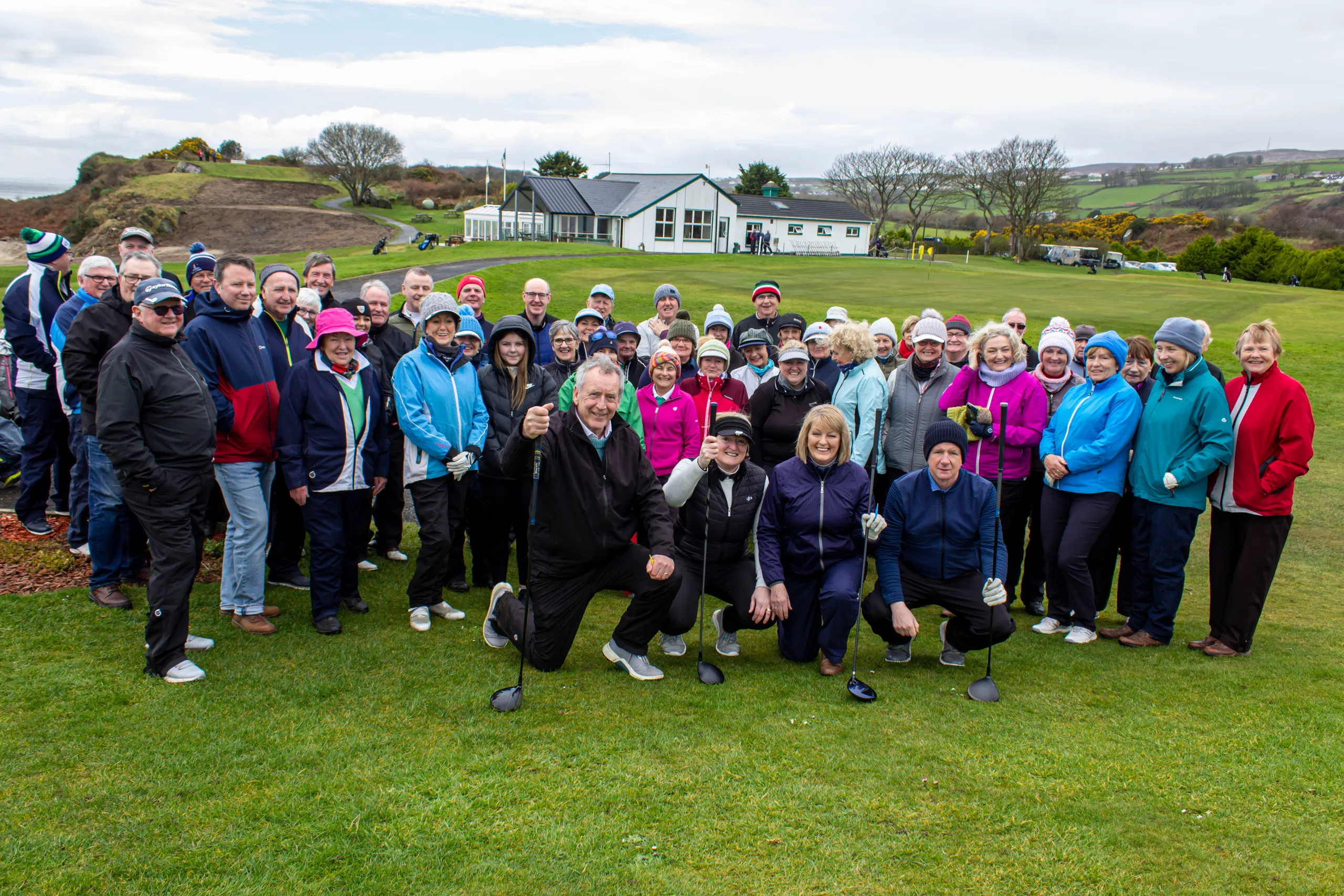Large group of golfers on the green by the clubhouse, smiling in winter gear at an Irish golf club.