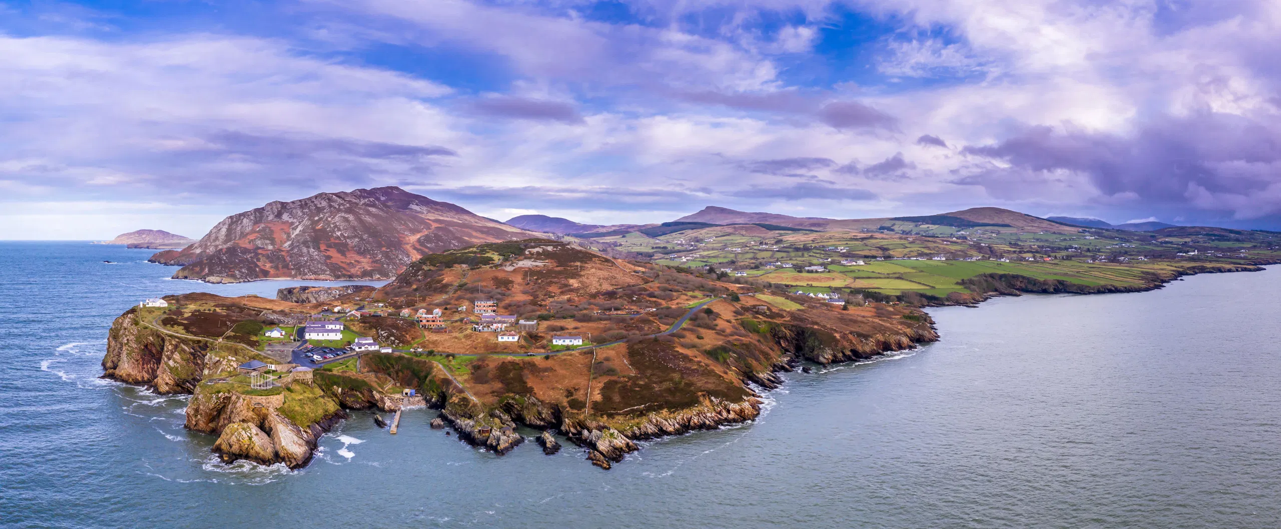 Rugged Irish headland on the Wild Atlantic Way, cottages on sea cliffs with waves and patchwork fields