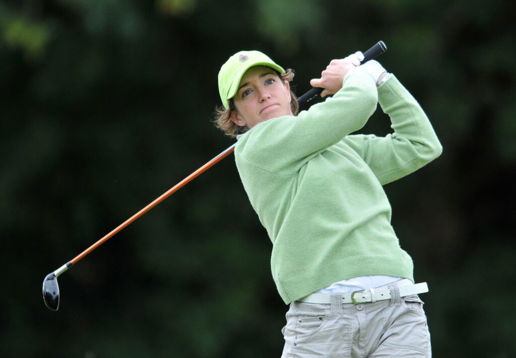 Woman golfer in a green jumper follows through on a tee shot
