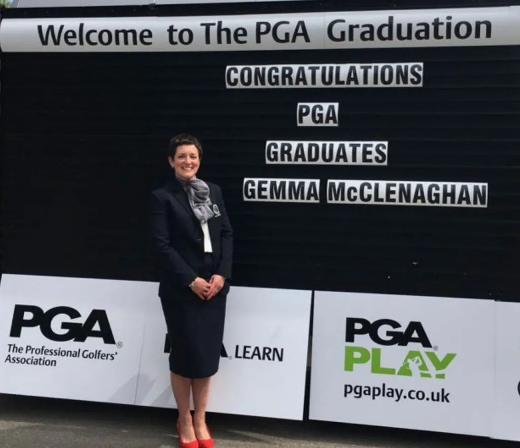 Smiling woman in a suit beside a Welcome to the PGA Graduation sign celebrating new PGA golf graduates.