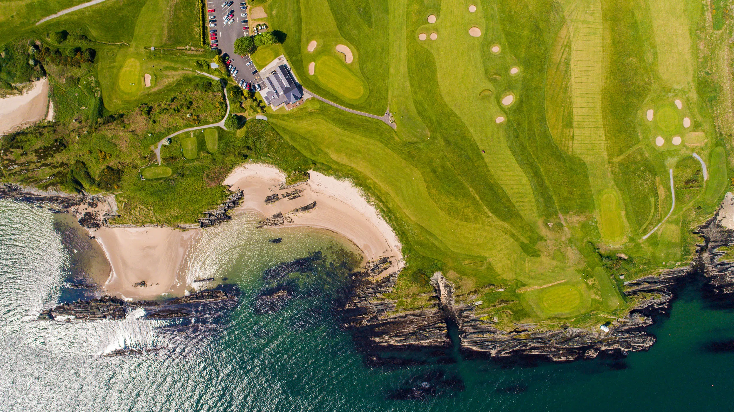 Aerial view of a seaside links golf course above sandy coves and rocky cliffs on Ireland’s Atlantic coast