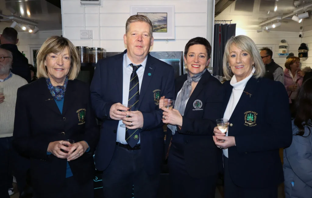 Four golf club members in navy blazers at a clubhouse event, smiling with drinks.