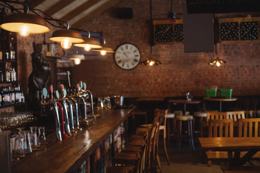 Cosy Irish pub bar with draught beer taps, warm pendant lights and wooden stools against a brick wall and clock.