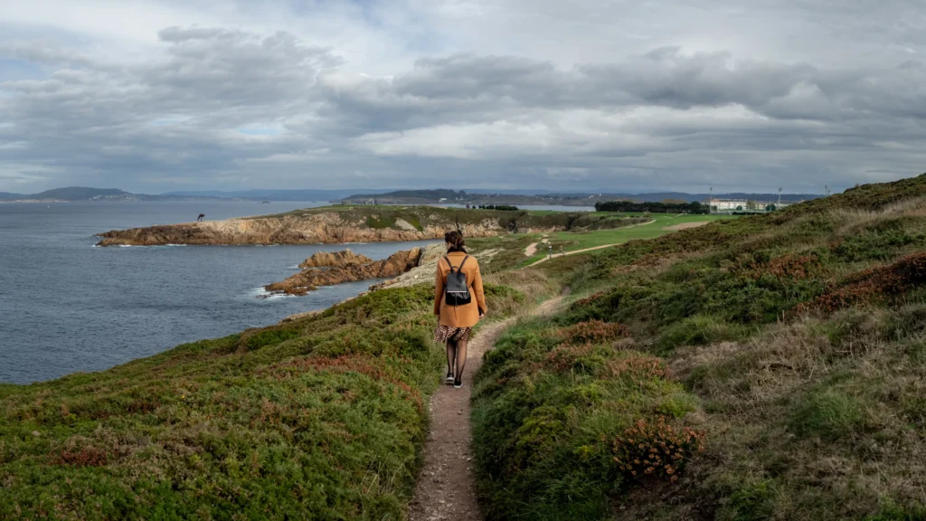 Walker with a backpack on a coastal path above rocky headlands, grey sea and brooding clouds.
