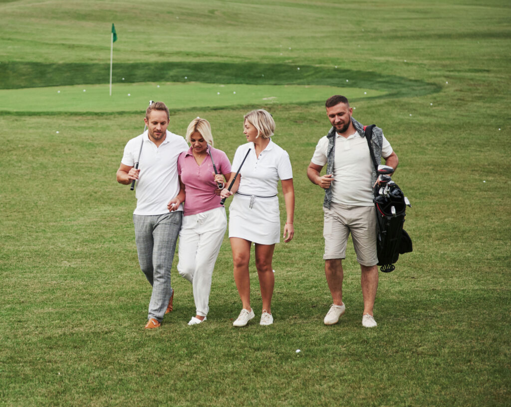 Four golfers stroll by the green, chatting and carrying clubs on a lush course