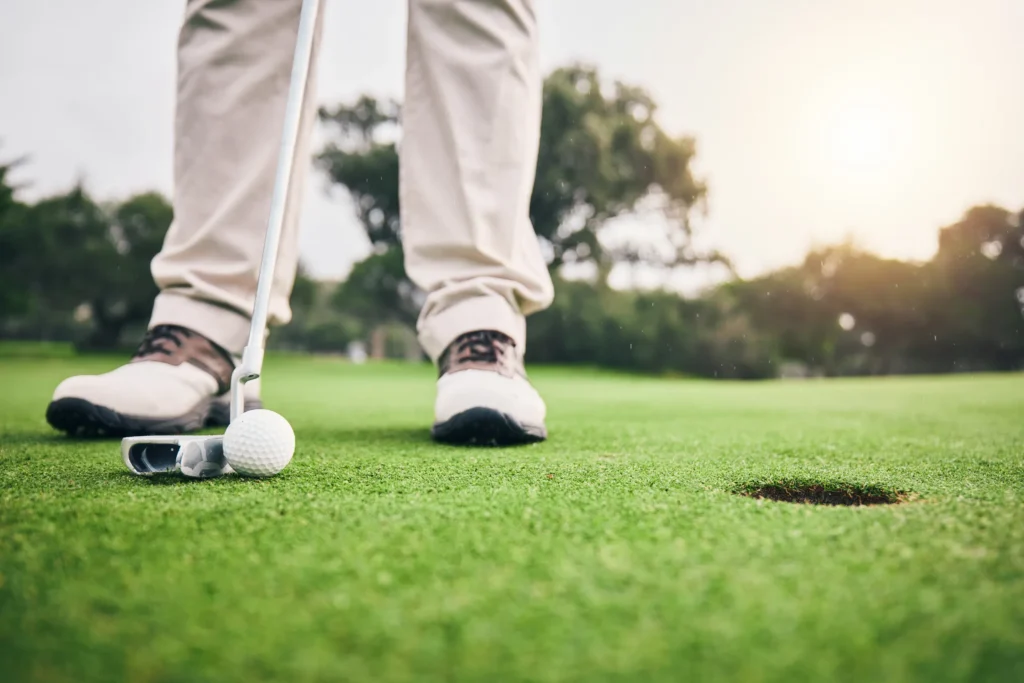 Golfer lining up a short putt on a sunlit green, ball and putter near the hole