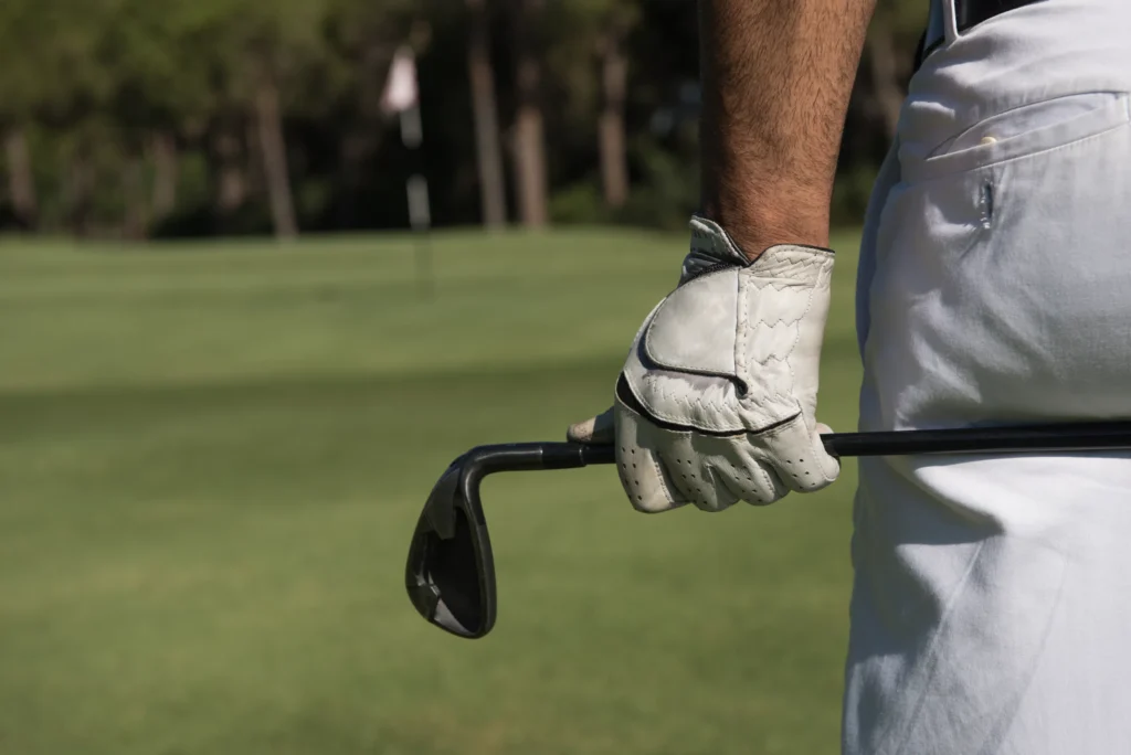 Gloved hand holds a bent golf iron near the green, the flag in the distance.