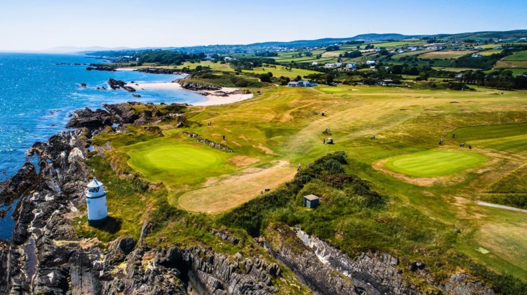Clifftop links golf course by the Atlantic in Ireland, with a white lighthouse, rocky shores and sandy coves.