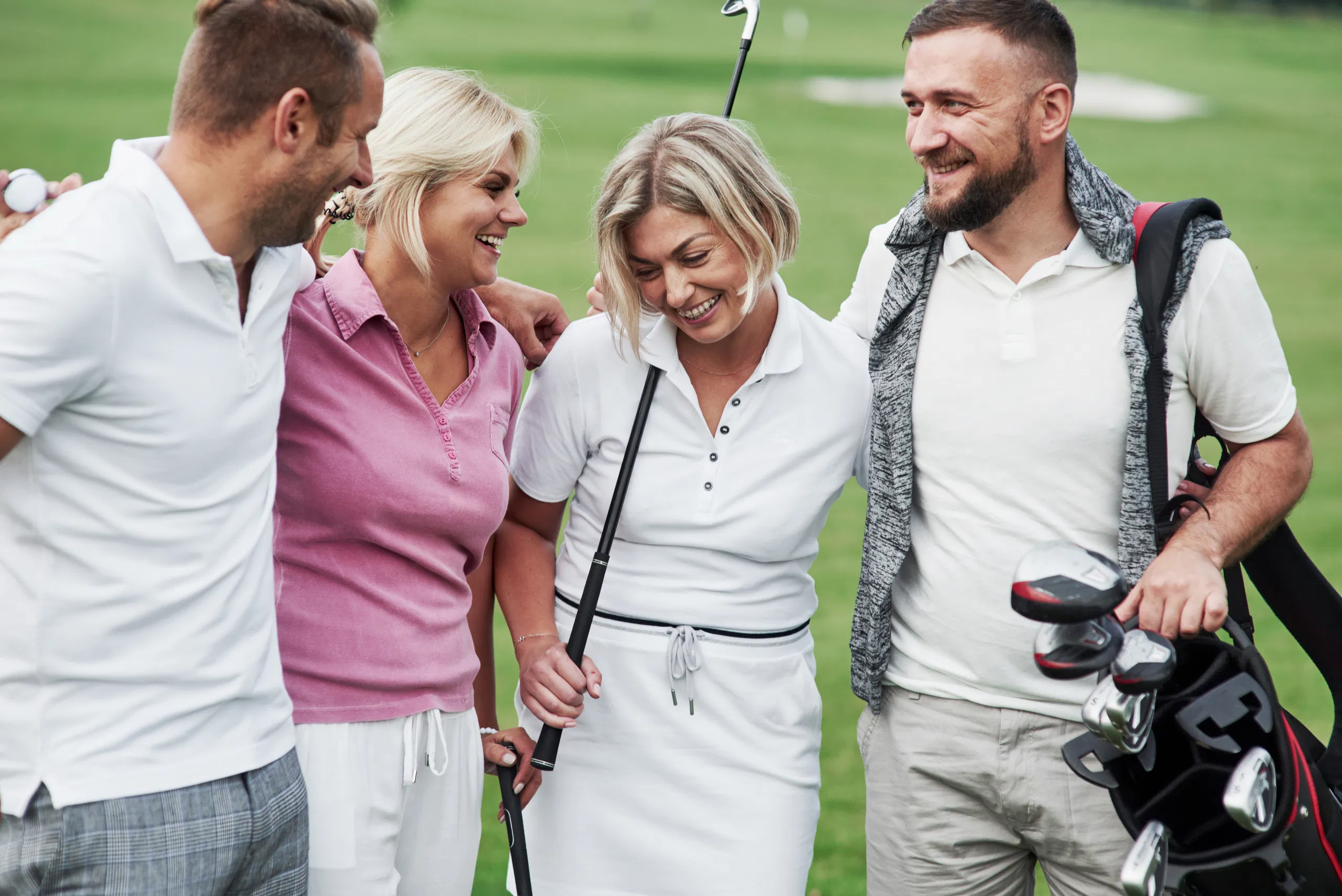 Four pals laughing on a golf course, golfers with clubs and a bag