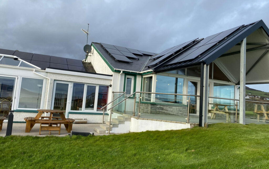 Coastal building with solar panels, glass veranda and picnic benches on a green lawn under grey skies