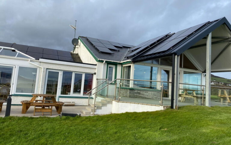 Coastal building with solar panels, glass veranda and picnic benches on a green lawn under grey skies