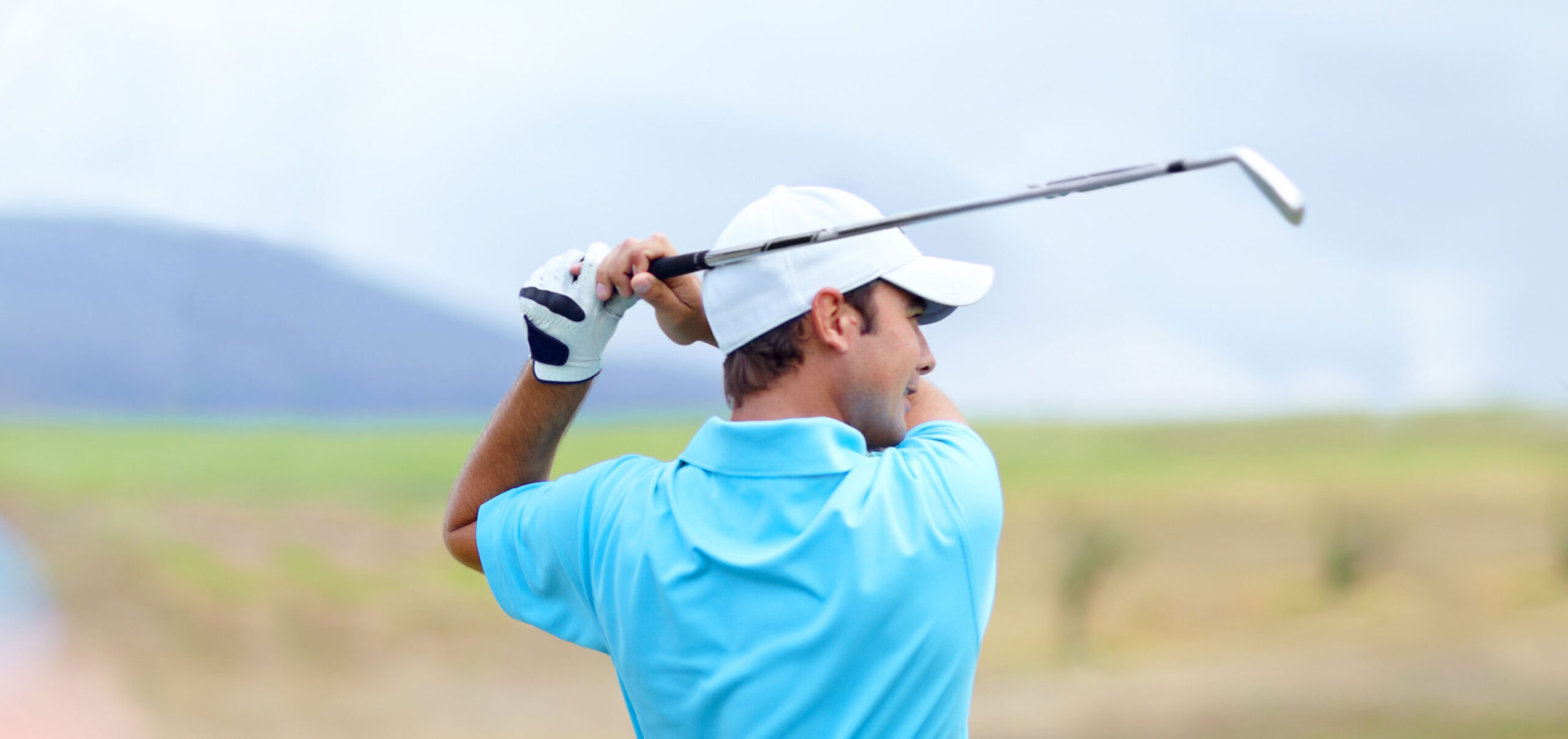 Golfer in a blue polo finishing a swing on a green golf course under a bright sky
