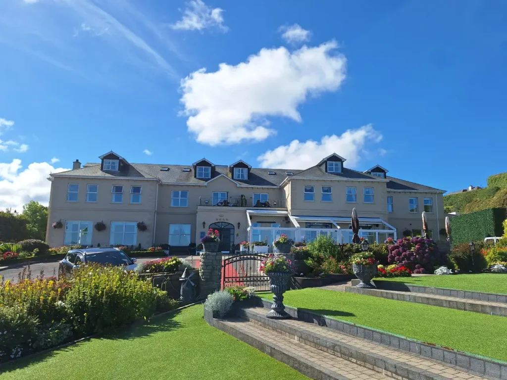 Elegant country house hotel with dormer windows and colourful gardens on a bright blue-sky day.