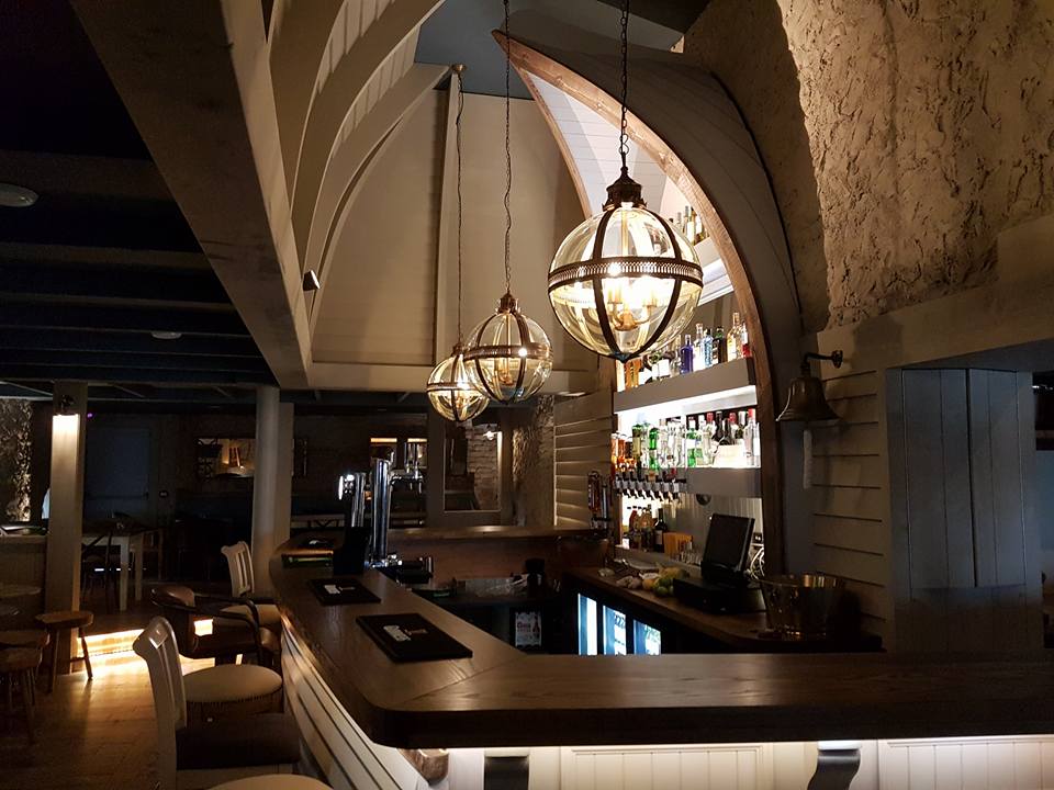 Cosy Irish pub bar with globe pendant lights, arched ceiling, wooden counter and shelves of spirits
