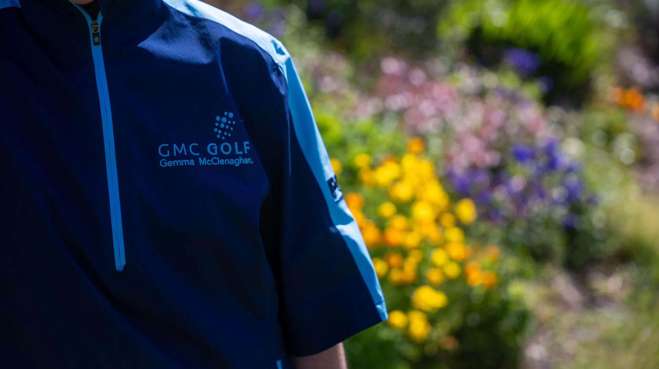 Blue GMC Golf jacket with name visible, set against a colourful blurred garden background.