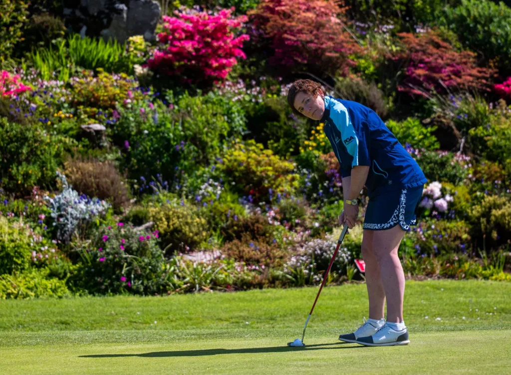 Golfer preparing to putt on a vibrant green course with colourful flowers in the background.