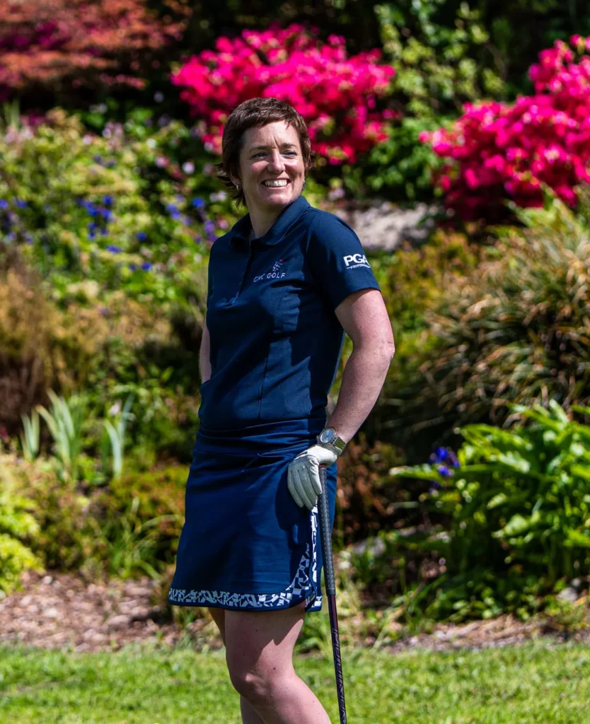 Smiling golfer in blue attire stands on a sunny course, vibrant flowers in the background.