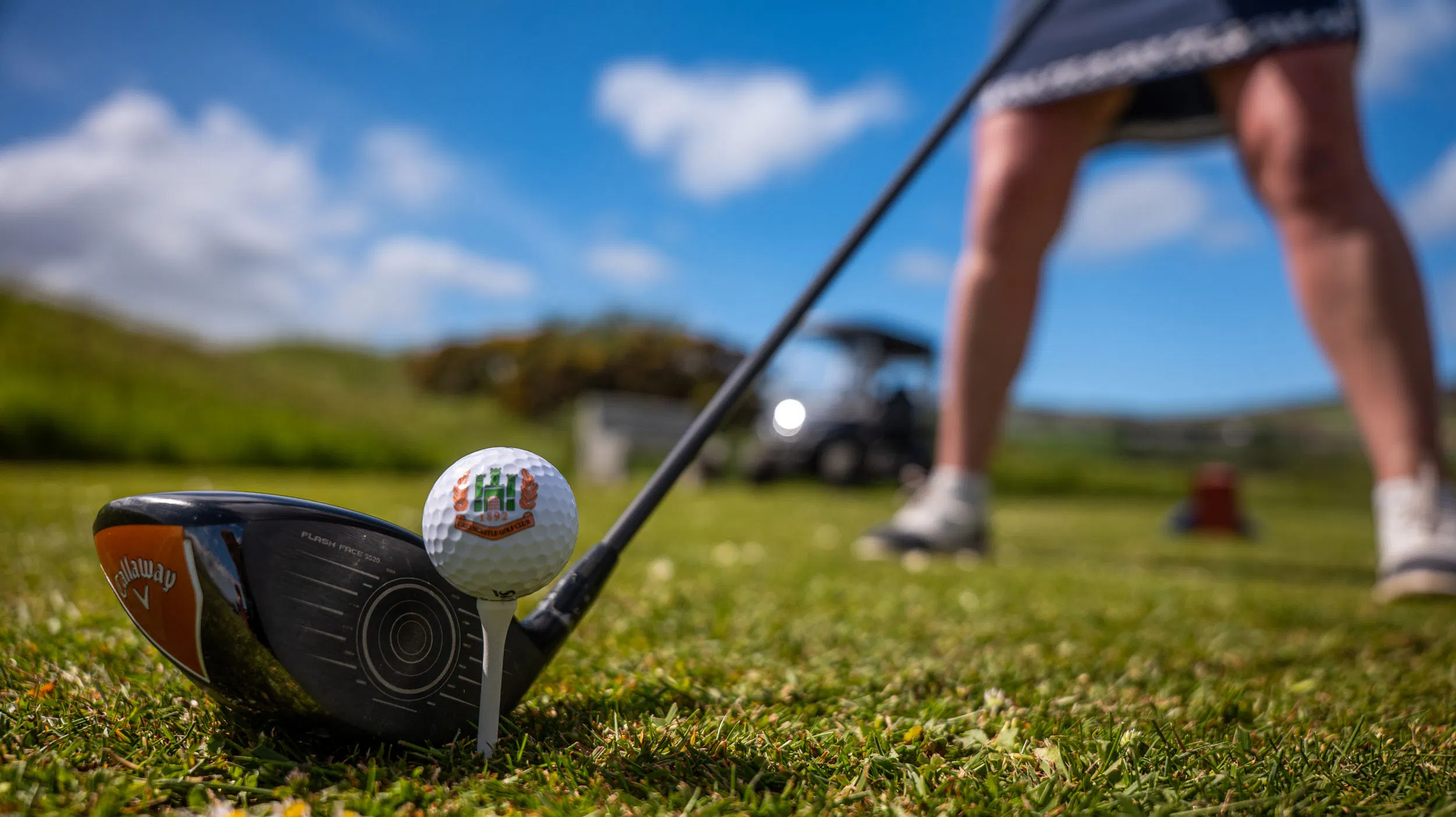 Golf club poised to hit a ball on a sunny course with golfer ready to swing.